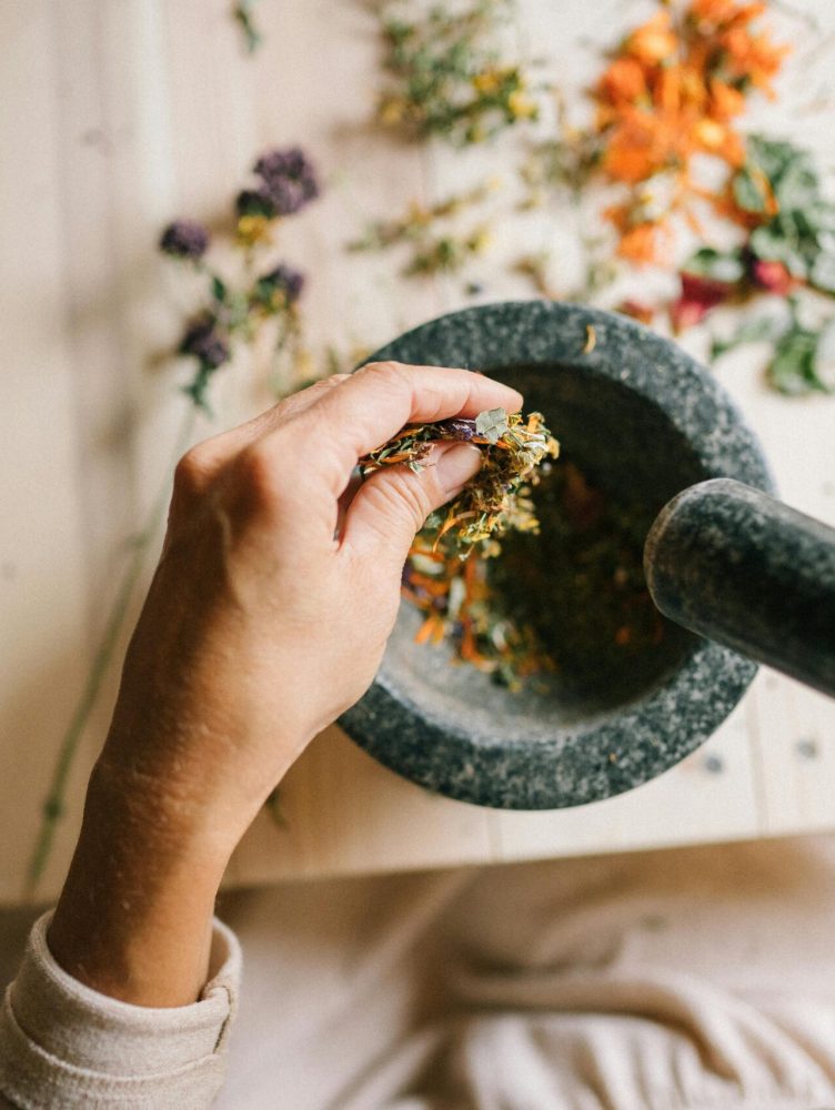 Top view of hands grinding dried herbs using a mortar and pestle on a wooden table.